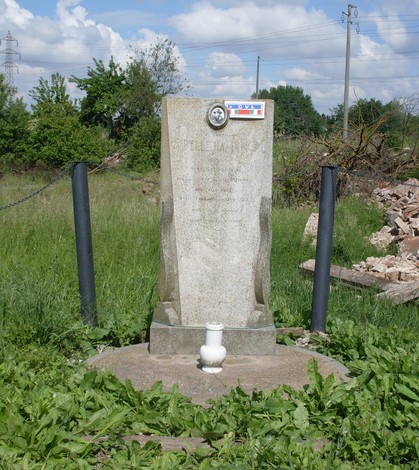 Cippo a Bellesia, monumento in pietra circondato da verde e resti di costruzioni.