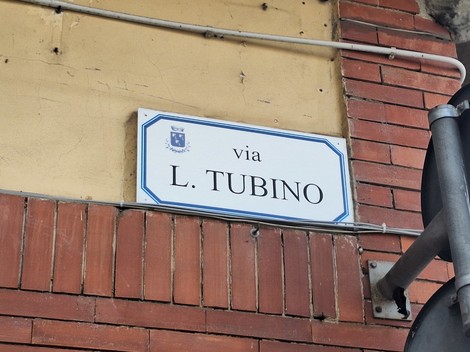 Insegna stradale con il nome della via L. Tubino su un edificio con mattoni a vista.