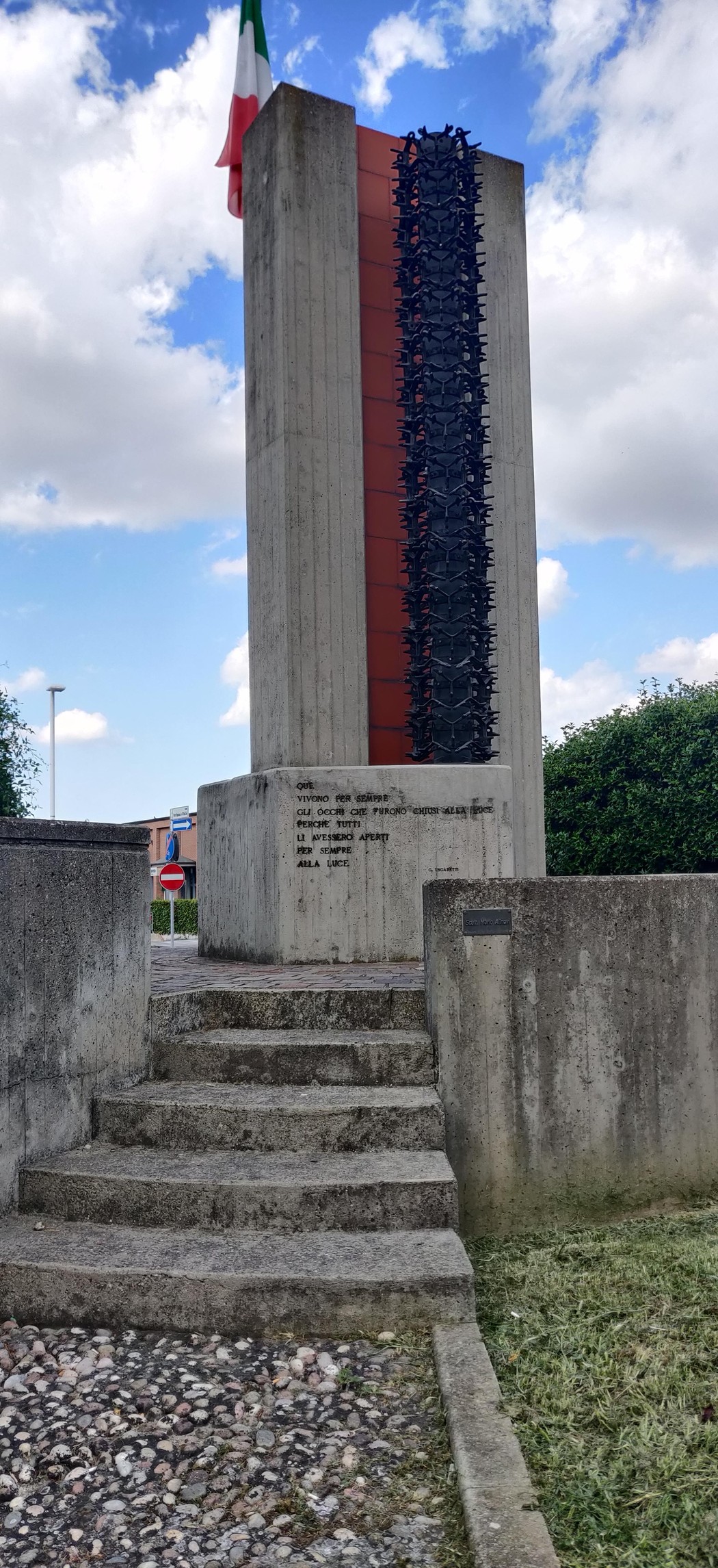 Monumento ai partigiani, una stele in cemento con bandiera italiana, simbolo di memoria storica e resistenza.