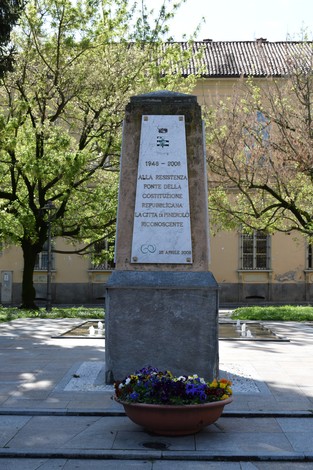 Monumento alla Resistenza con iscrizione commemorativa, circondato da un giardino fiorito e alberi.