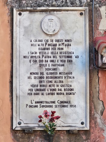 Lapide commemorativa della Resistenza con fiori, situata in un contesto urbano.