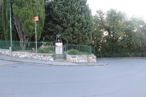 Monumento ai caduti circondato da alberi e una recinzione su un angolo di strada tranquillo.