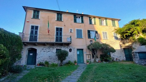Edificio storico con facciata color pastello, balconi, finestre con persiane e giardino curato.
