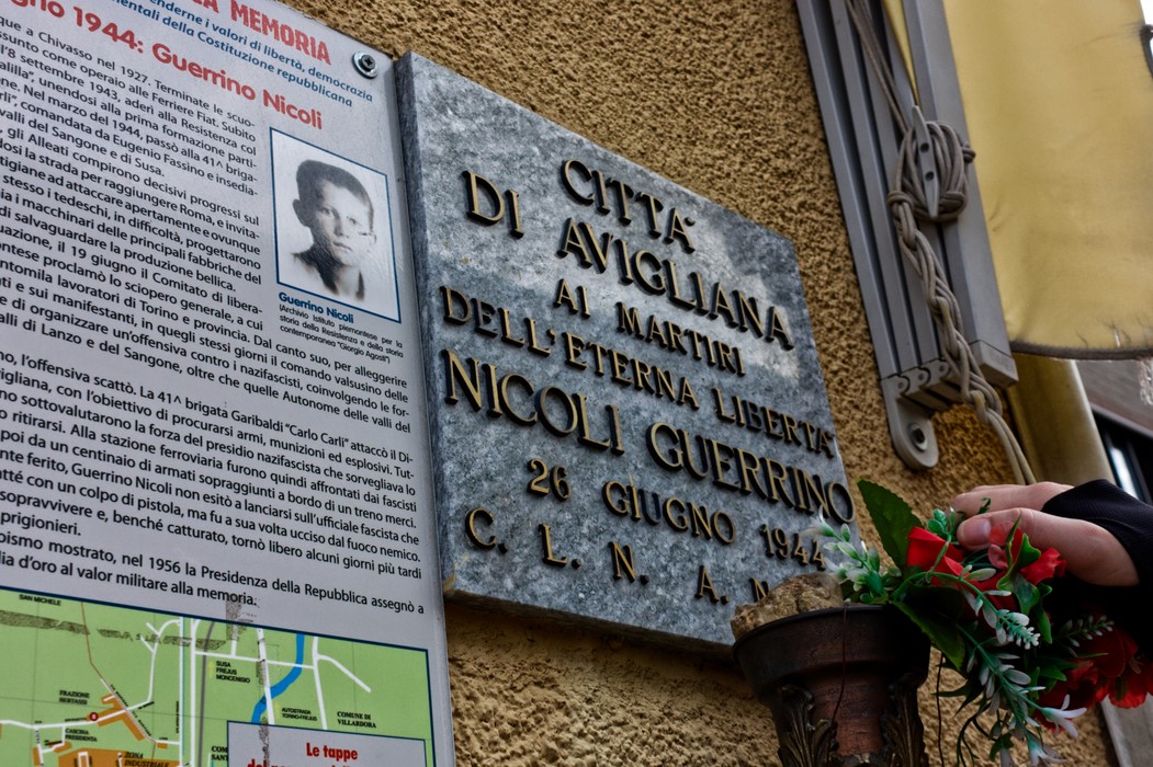 Lapide commemorativa dedicata a Nicoli, simbolo di libertà a Avigliana, con omaggi floreali.