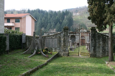 Monumento del cimitero di Stia, con ingresso in ferro battuto e un ambiente naturale circostante.
