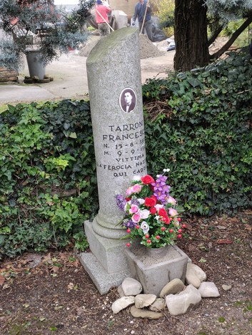 Cippo commemorativo a Tarroni, con fiori in omaggio e un'immagine in ceramica. Rappresenta la memoria storica locale.