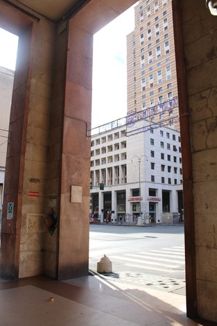 Vista architettonica di un ingresso, con un traforo che affaccia su una strada urbana e edifici moderni sullo sfondo.