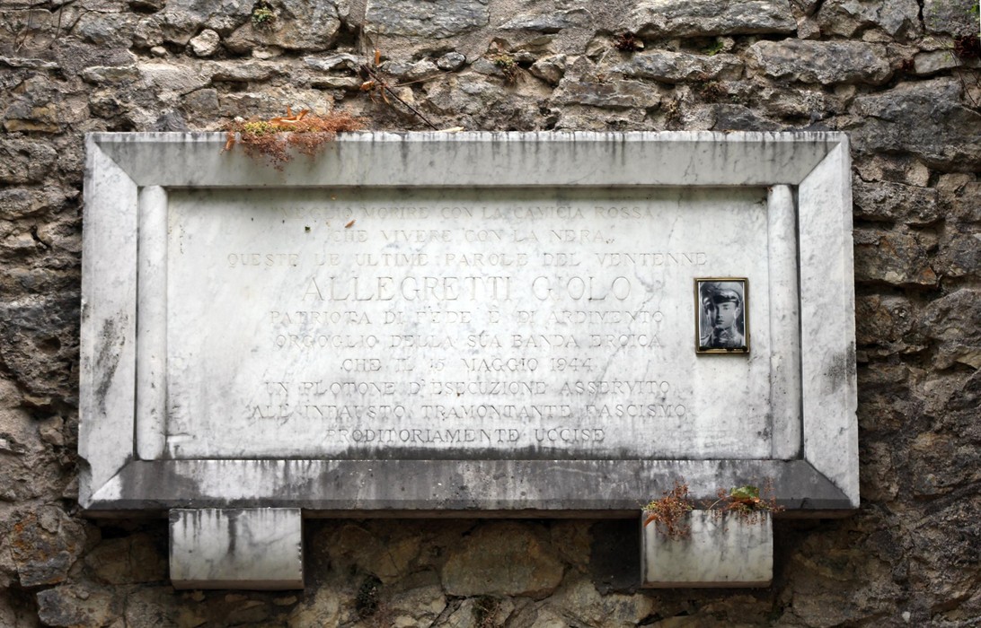 Lapide commemorativa ad Allegretti, incastonata in una parete di pietra, con evidenti segni di usura.