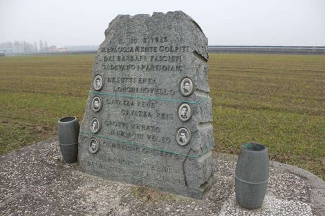 Cippo commemorativo in pietra dedicato a Besutti, Longhi e altri, situato in un campo.