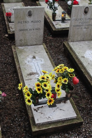 Tombe bianche adornate con fiori gialli, dedicate ai caduti per la Libertà. Atmosfera di rispetto e memoria.
