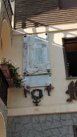 Lapide commemorativa con nomi di caduti, decorata con elementi floreali e artistiche sculture in bronzo.