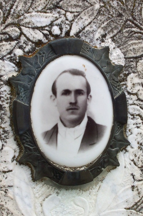 Ritratto in ceramica di un uomo su una tomba, incorniciato da ornamenti funerari.