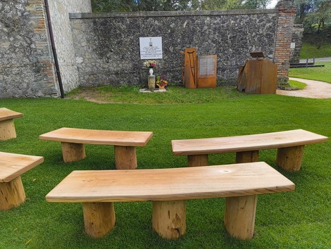 Area relax con panche in legno, circondata da natura e un'illustrazione commemorativa. Perfetta per pause tranquille.