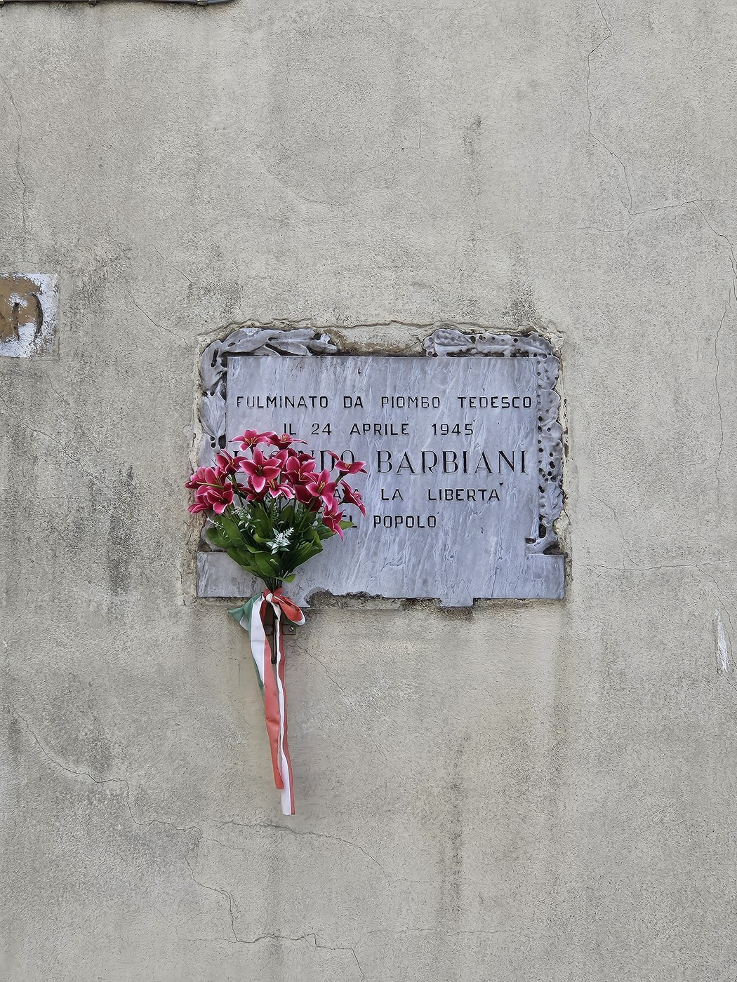 Lapide commemorativa con fiori, in ricordo di Barbiani, vittima di un attacco nel 1945.