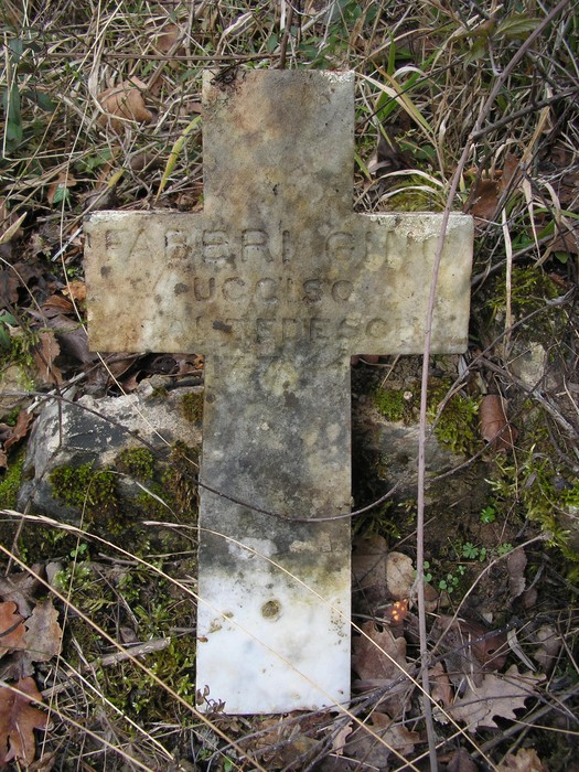 Cippo commemorativo con croce, immerso nella vegetazione e segnato dal tempo.