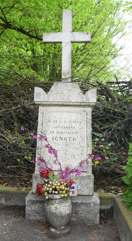 Cippo commemorativo dedicato a un partigiano ignoto, con fiori e simboli di onore e memoria.