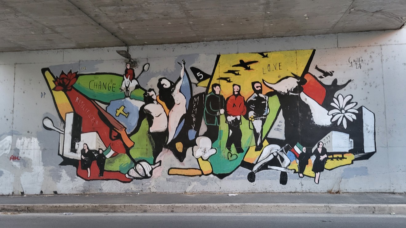 Murale "Le ali della memoria" che unisce simboli di cambiamento, amore e pace su un muro urbano.