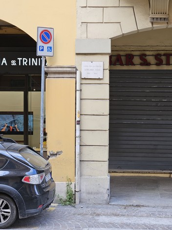 Lapide a Tosi situata su una parete di edificio, accanto a un'automobile parcheggiata.