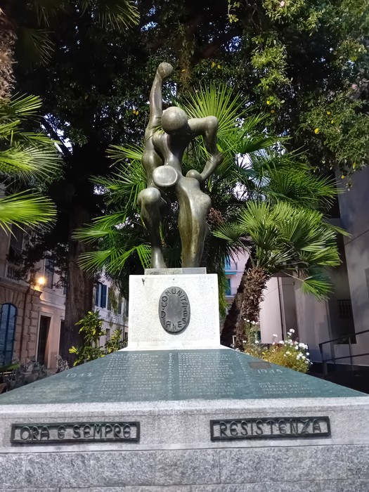 Monumento alla Resistenza con figure bronzee, circondato da vegetazione, simbolo di lotta e libertà.