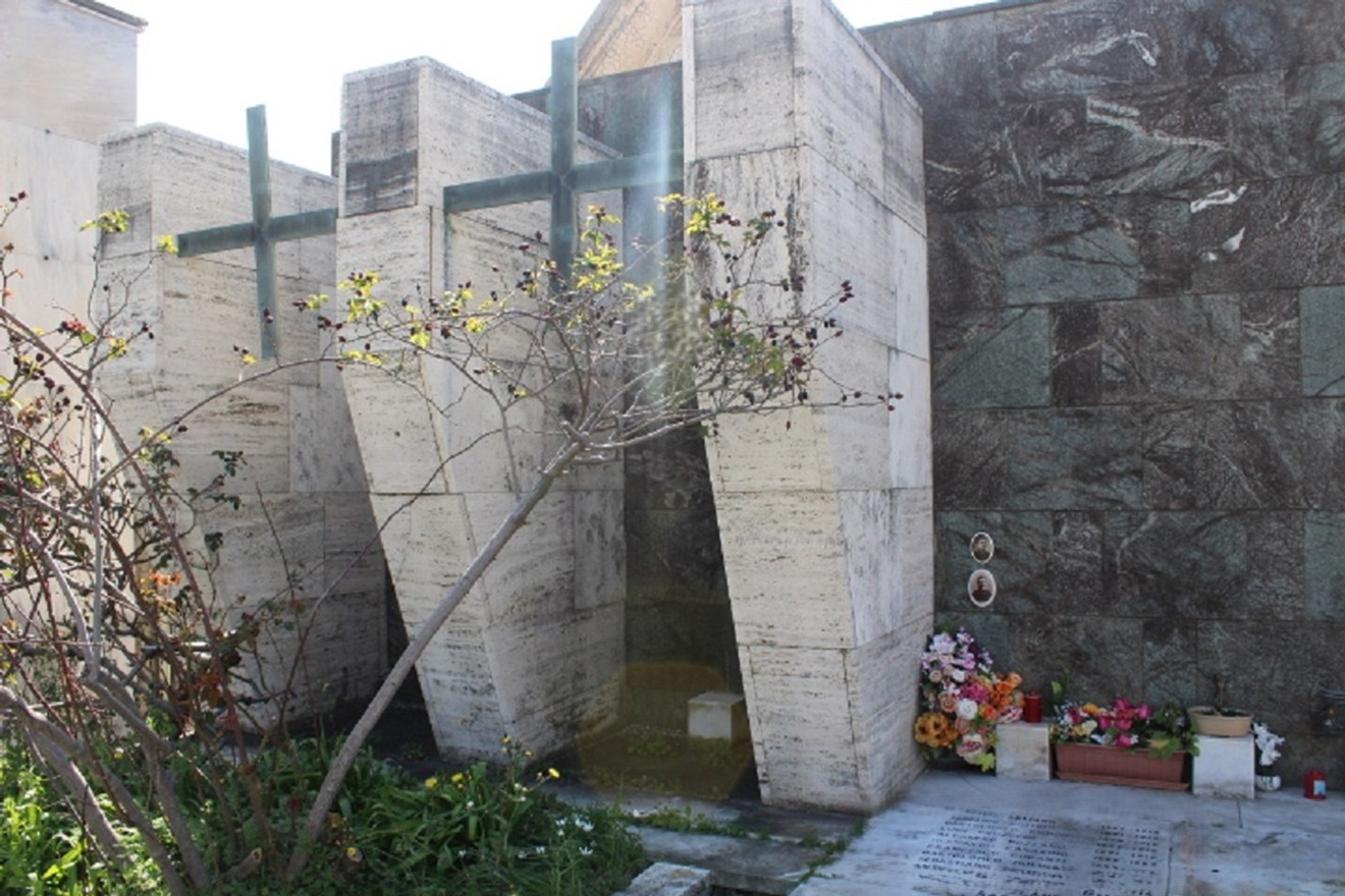 Monumento ai caduti di Palmaro, struttura moderna con elementi verticali e decorazioni floreali circostanti.