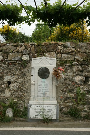 Monumento dedicato a Casini, con un busto e decorazioni floreali, situato in un paesaggio verde.
