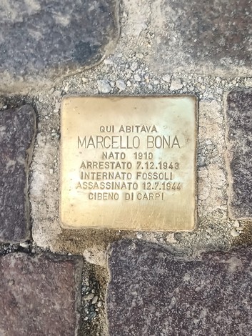 Pietra d'inciampo in ottone incastonata tra i sampietrini, con iscrizione incisa.