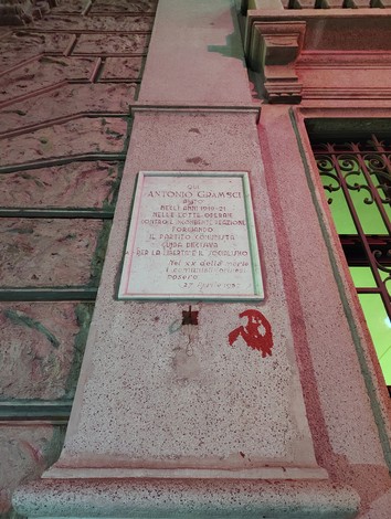 Lapide commemorativa ad Antonio Gramsci affissa su un muro, con dettagli architettonici circostanti.