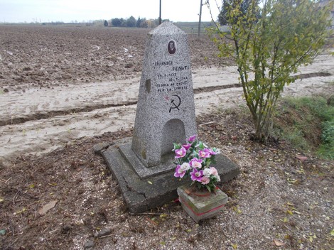 Cippo memoriale dedicato a Fenati, con fiori e un paesaggio rurale circostante.