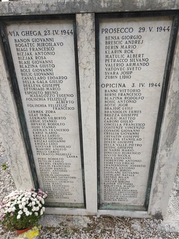 Una stele commemorativa dedicata ai caduti per la libertà, con nomi incisi e fiori ai piedi.