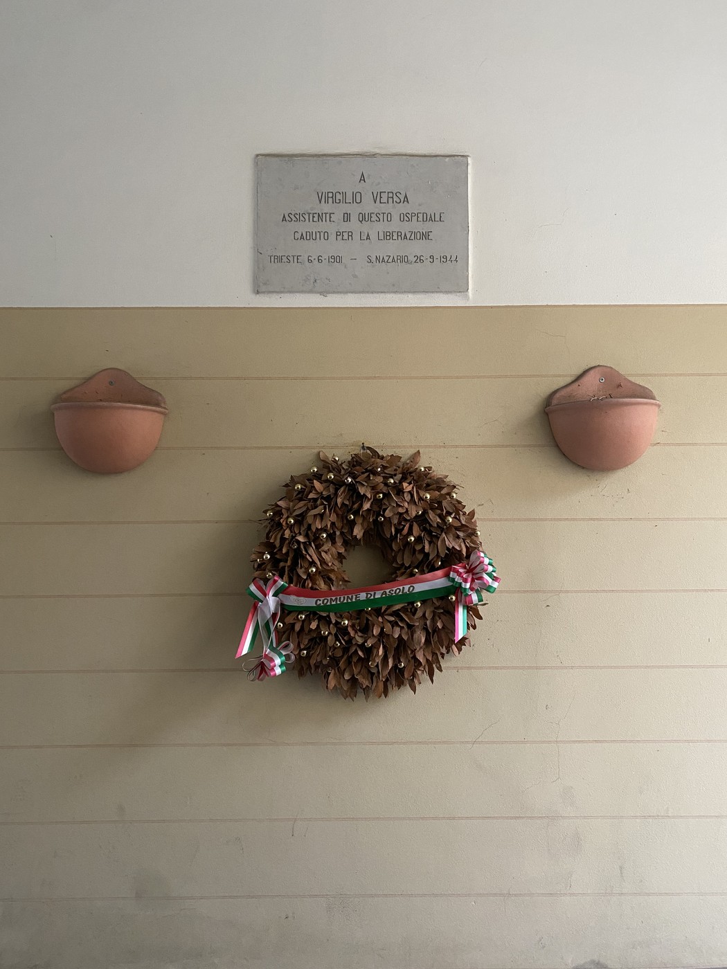 Lapide commemorativa dedicata a Virgilio Versa, con una corona di alloro decorata.