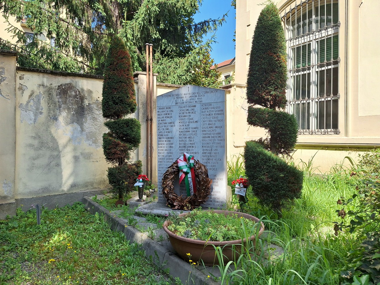 Monumento dedicato ai Martiri della Libertà, circondato da alberi e decorazioni floreali, in un'area verde.