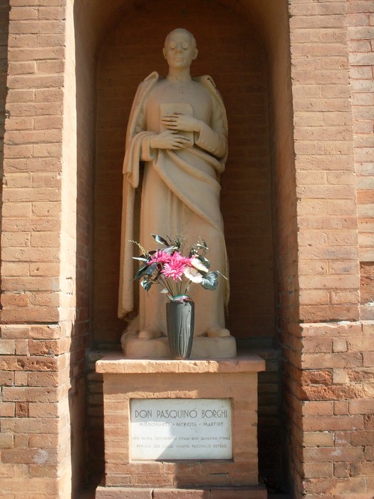 Statua di Pasquino Borghi, con fiori e dedica su base, esposta in un angolo di un edificio.