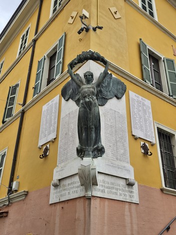 Monumento commemorativo ai caduti con statue e iscrizioni su una parete gialla di un edificio.