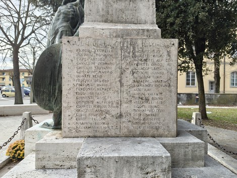 Monumento ai caduti con iscrizioni in memoria delle persone combattute, circondato da alberi e un'atmosfera commemorativa.