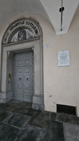 Lapide commemorativa presso l'ingresso dell'Asilo Infantile Cittadino, con porta e architettura storica.