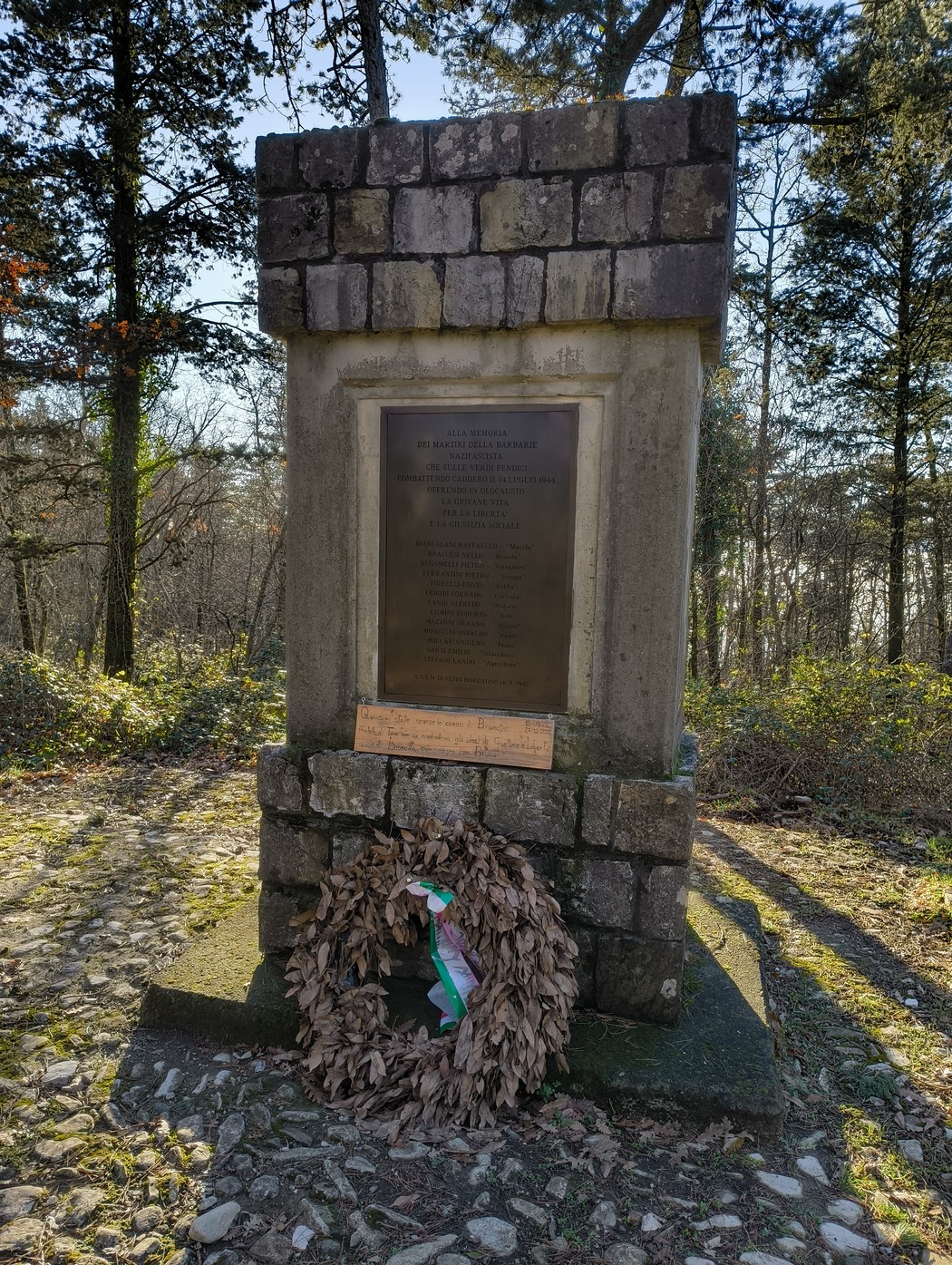 Monumento commemorativo della Battaglia della Fonte dei Seppi, circondato da natura e un omaggio floreale.