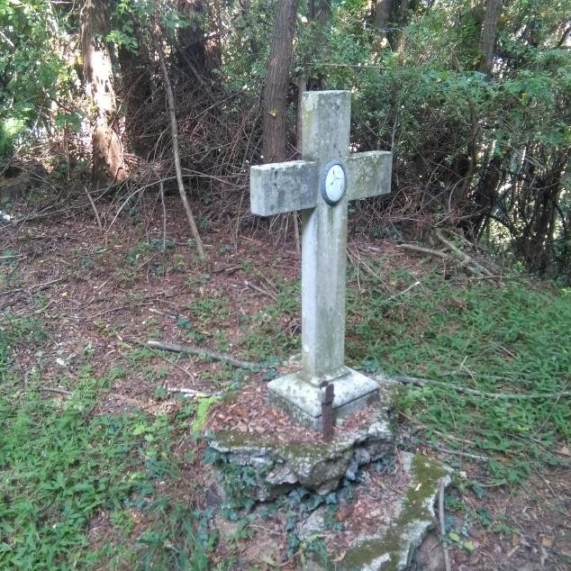 Croce in pietra situata nel verde, simbolo di ricordo e spiritualità nel contesto naturale circostante.