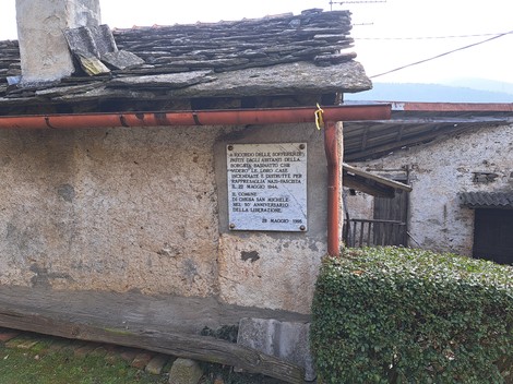 Lapide commemorativa dedicata all'incendio della Borgata Basinatto, affissa su un edificio rurale.