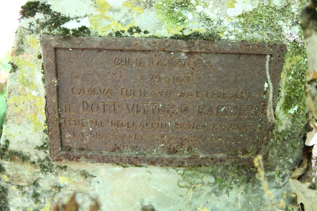 Cippo commemorativo dedicato a Vittorio Barbieri, situato in una zona boschiva.