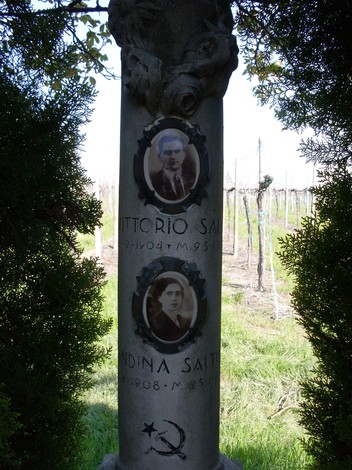 Cippo commemorativo con ritratti di Vittorio e Lindina Saltini, circondato da verdeggiante natura.