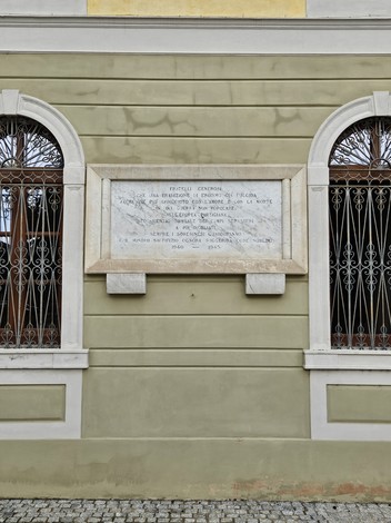 Lapide commemorativa dedicata ai caduti per la libertà, situata su una parete con finestre ornate.