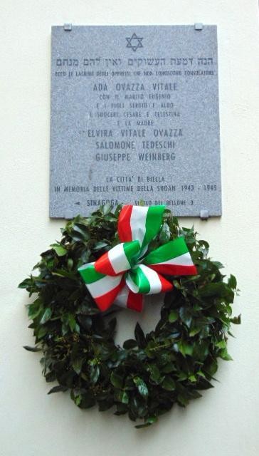 Lapide commemorativa dedicata alle vittime della Shoah, con corona di alloro e colori della bandiera italiana.