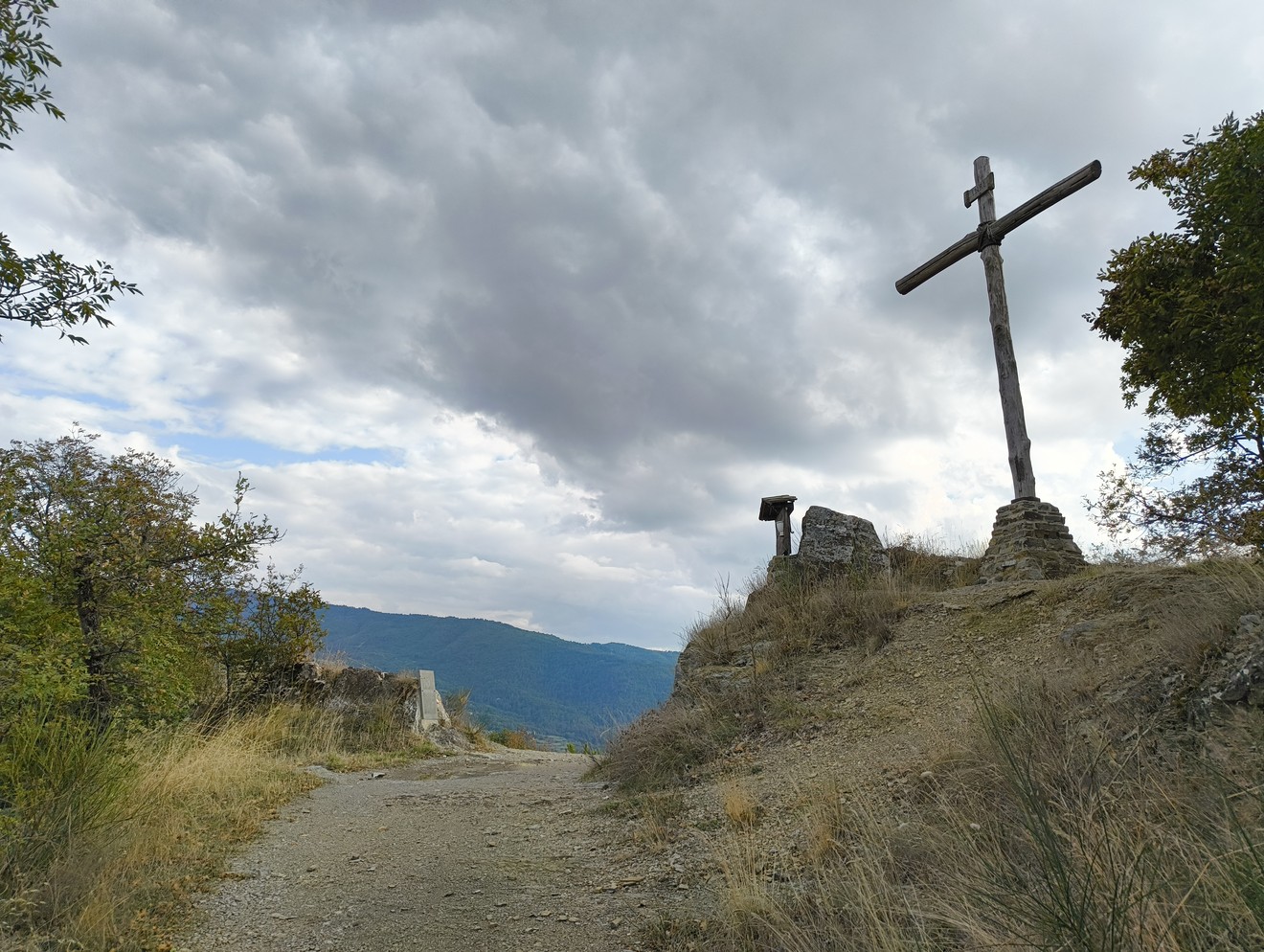 Lapide commemorativa per l'eccidio di Capraia, con croce in legno e paesaggio montano sullo sfondo.