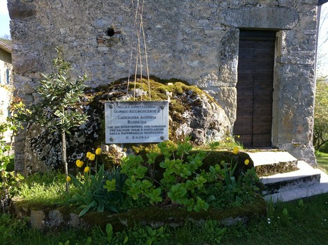 Lapide commemorativa a Ludescher e Roser, situata presso un edificio storico con vegetazione circostante.