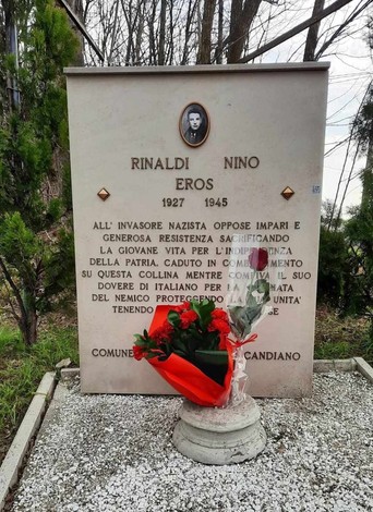 Monumento a Rinaldi Eros, giovane eroe caduto per la libertà, con fiori e segni di rispetto.
