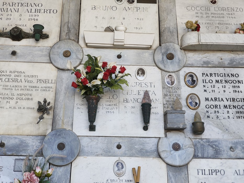 Lapidi marmoree di partigiani con foto ovali e iscrizioni, decorate da fiori e rosoni in pietra.