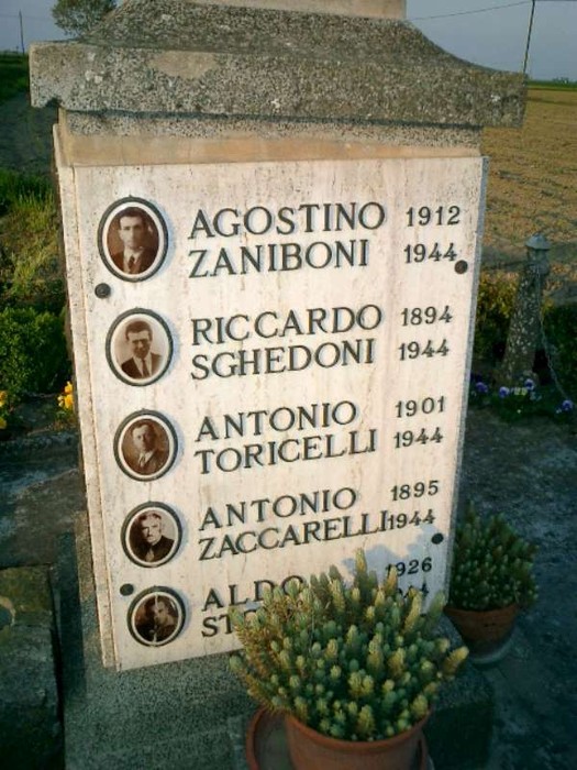 Monumento commemorativo con nomi di lavoratori coatti uccisi, incastonato in un paesaggio rurale.