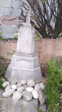 Cippo commemorativo in pietra dedicato ai partigiani, circondato da sassi e vegetazione.