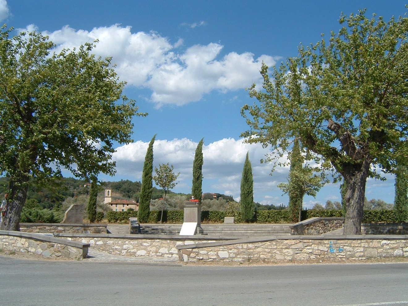 Area monumentale di Sant'Andrea, con alberi e un panorama sereno, incorniciata da un cielo nuvoloso.