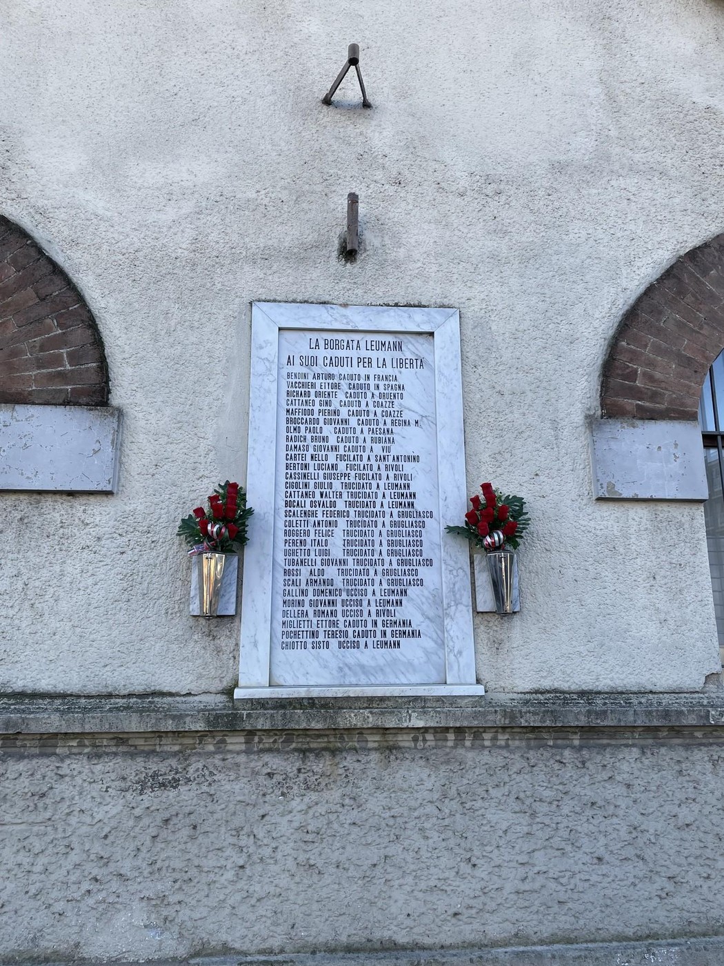 Lapide commemorativa ai caduti di Leumann, decorata con fiori, in onore dei sacrifici durante il conflitto.
